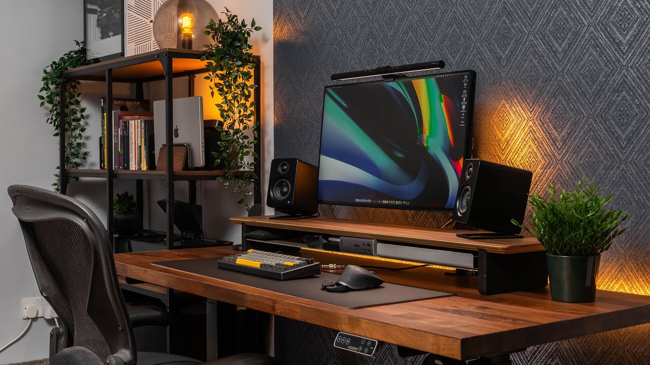 Modern wooden desk with monitor, speakers, plants, and ambient lighting