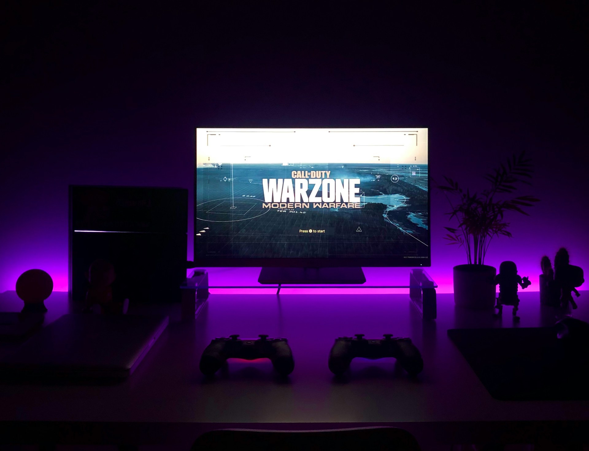 Gaming desk with Call of Duty: Warzone on screen, purple backlighting, two controllers